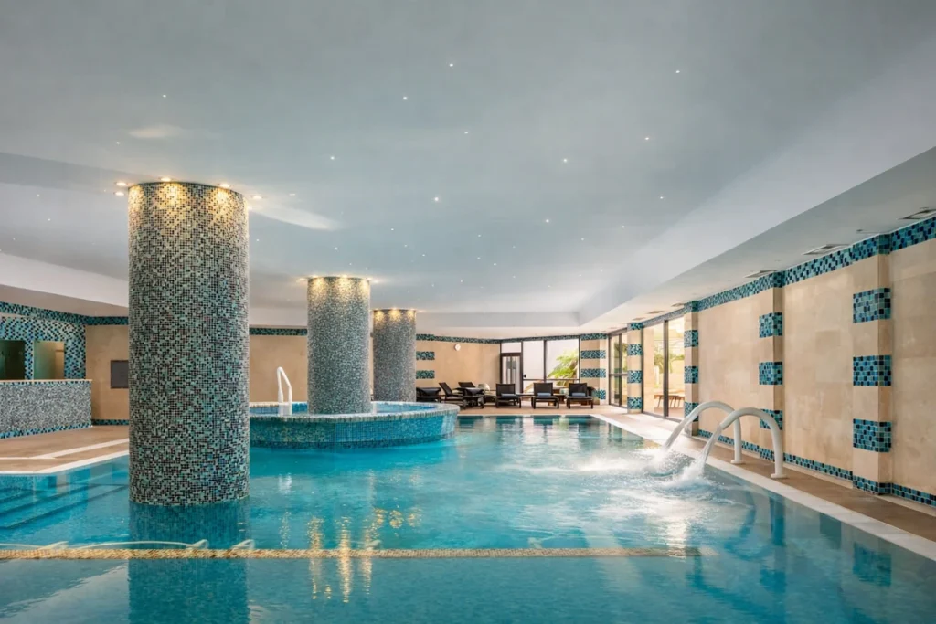 Indoor heated seawater pool with hydrotherapy jets at Grande Real Santa Eulália Resort & Hotel Spa in Albufeira, featuring mosaic-tiled columns and marine-based spa facilities.
