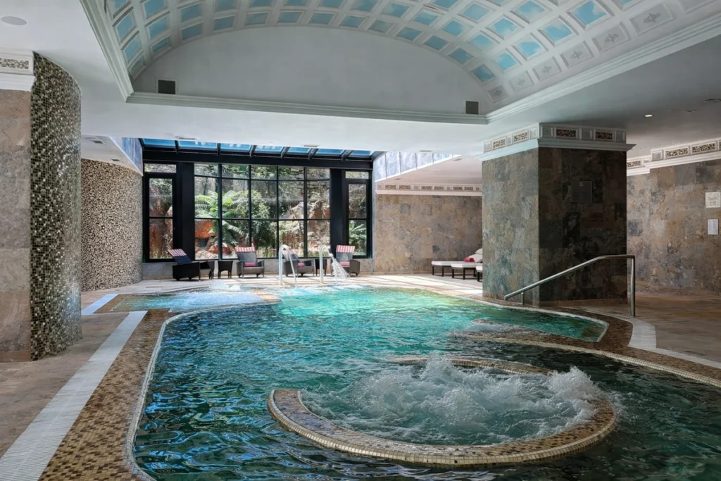 Indoor heated seawater pool with hydrotherapy jets at Grande Real Villa Itália Hotel & Spa in Cascais, featuring natural light, mosaic walls and marine-led spa facilities.